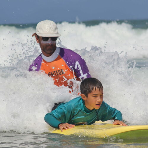 Photo d'un moniteur de surf qui guide un enfant sur une planche