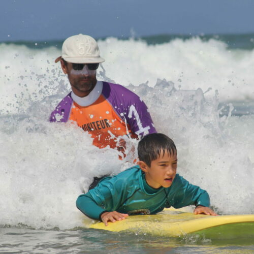 Photo d'un moniteur de surf qui guide un enfant sur une planche